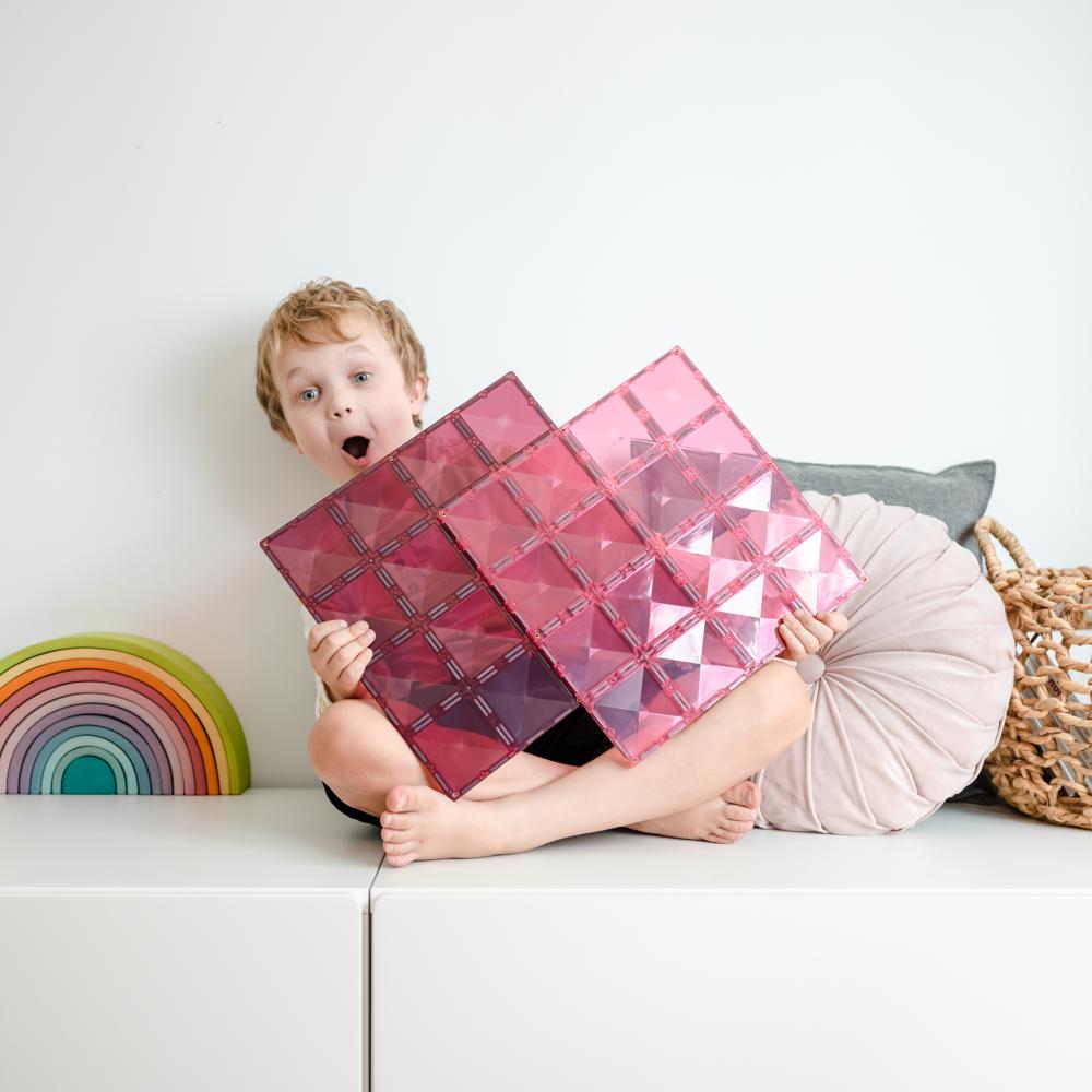 Child holding pink geometric blocks on a white surface