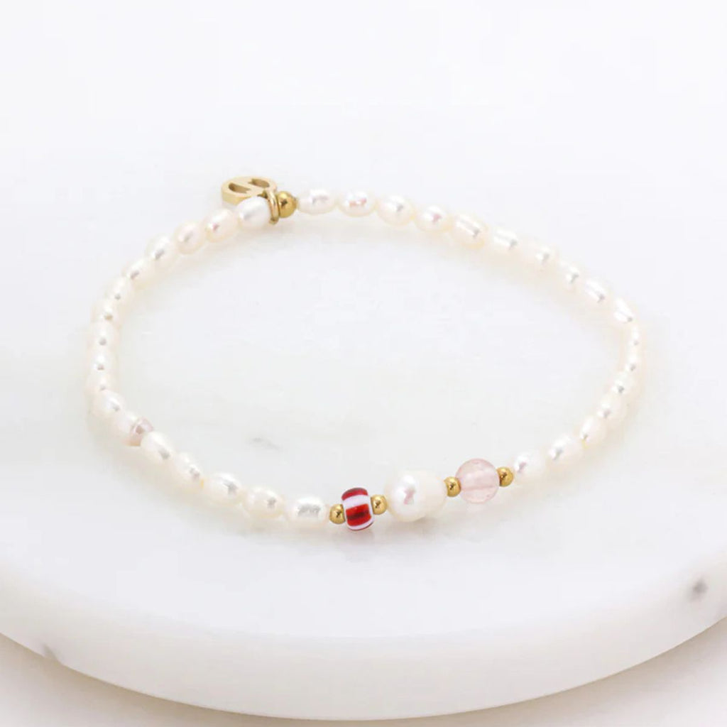 Pearl bracelet with gold and red beads on a white surface