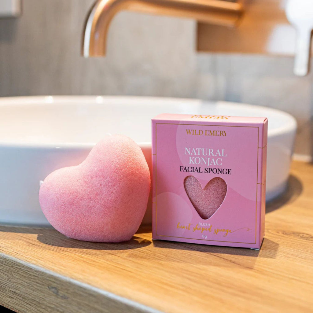 Pink heart-shaped facial sponge next to its packaging on a bathroom counter.