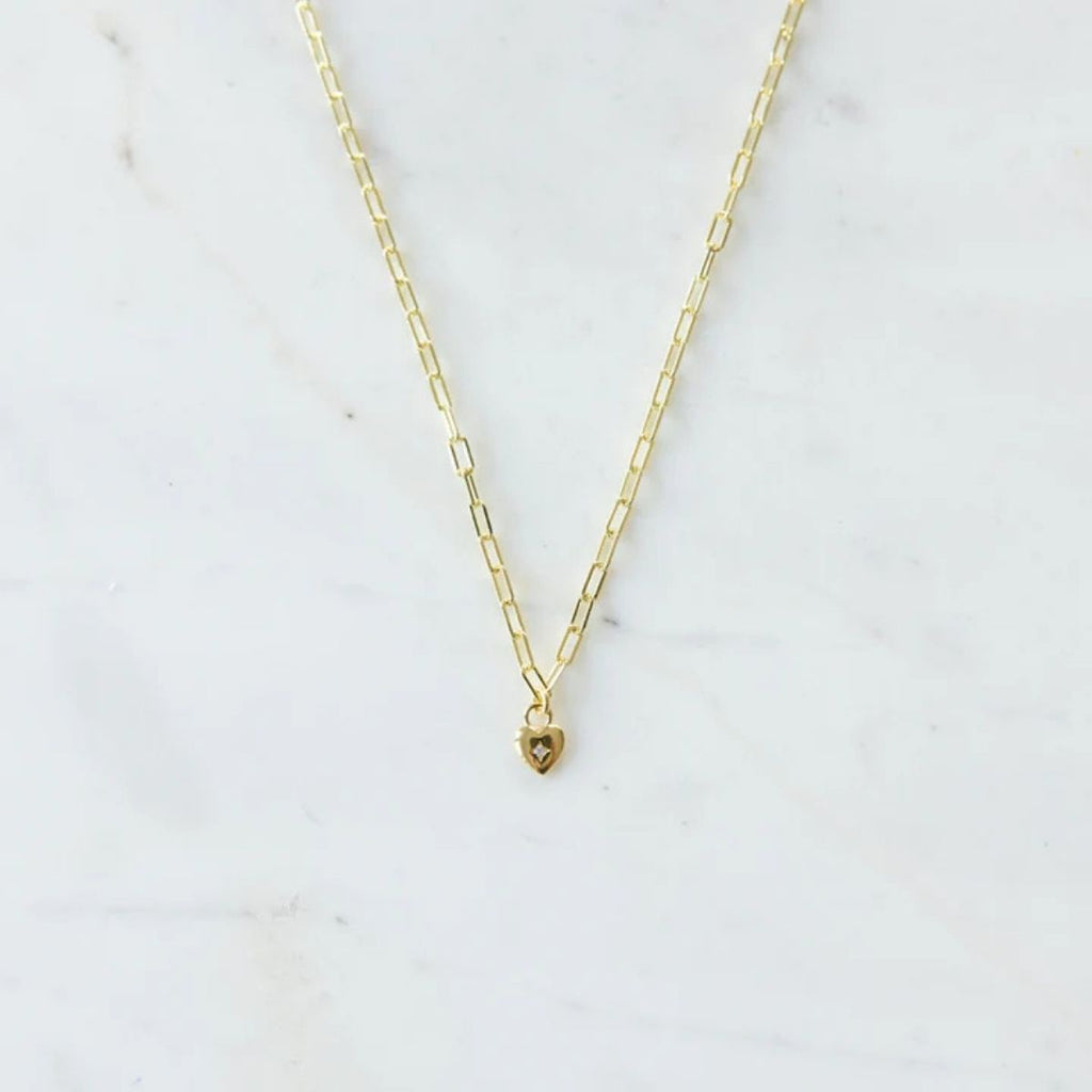 Gold necklace with a heart pendant on a white marble background