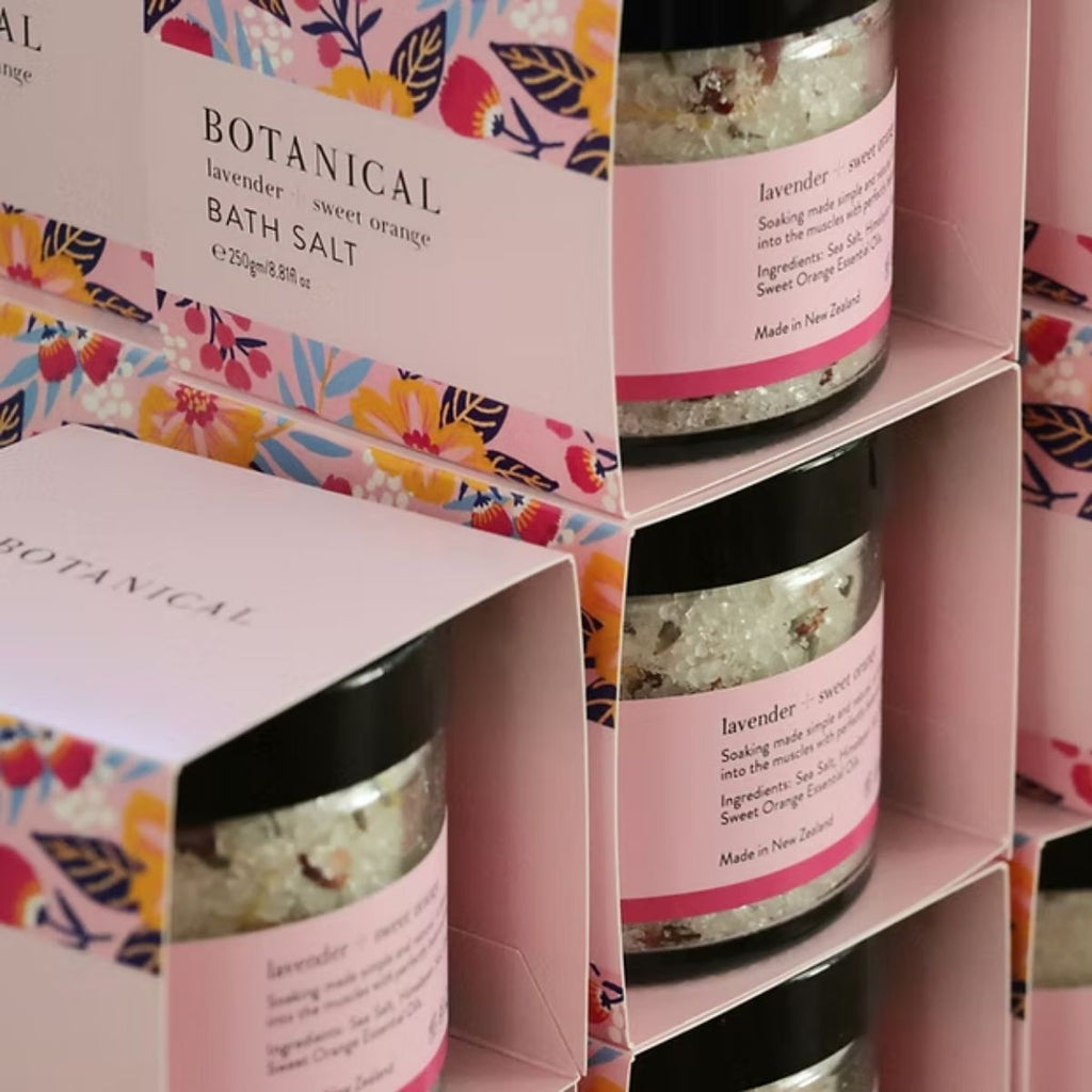 Bath salt packaging with floral design and pink labels on a pink display stand.