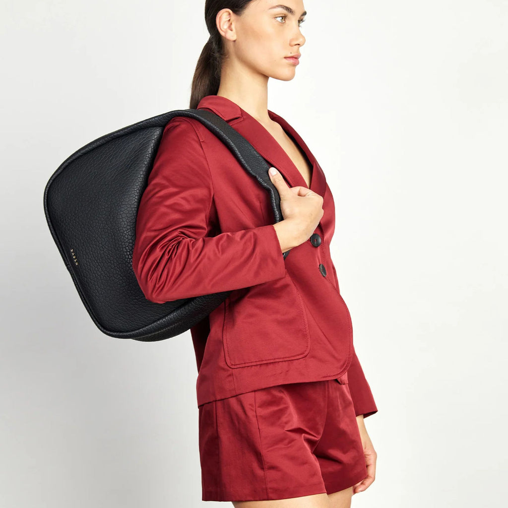 Person wearing a red blazer and shorts with a black handbag on shoulder