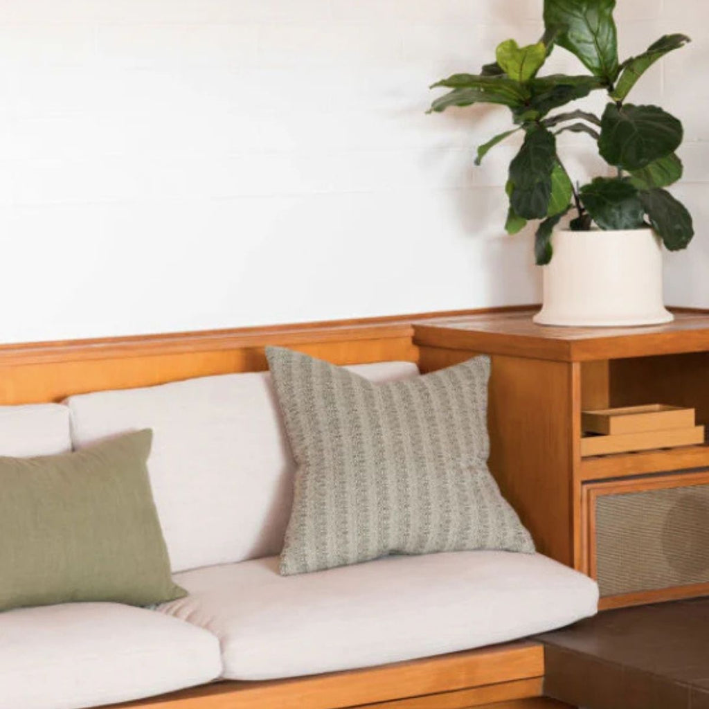Wooden bench with white cushions and green pillows, accompanied by a potted plant.