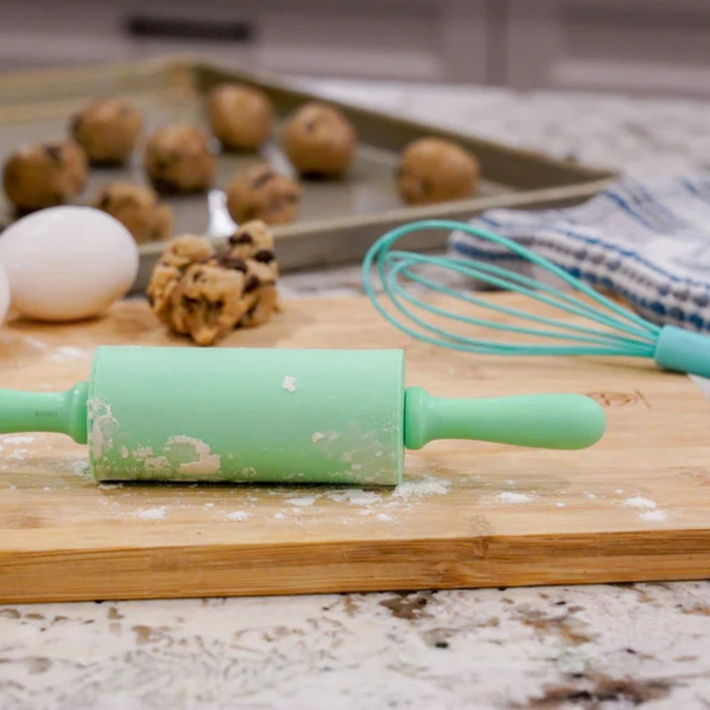 Green rolling pin on a wooden cutting board with baking ingredients in the background