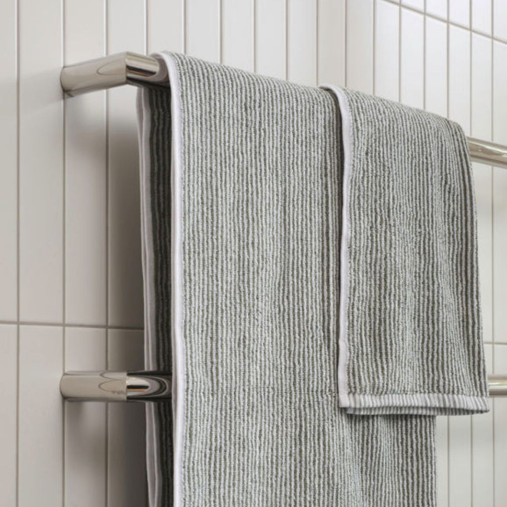 Gray textured towel hanging on a towel rack against a tiled bathroom wall.