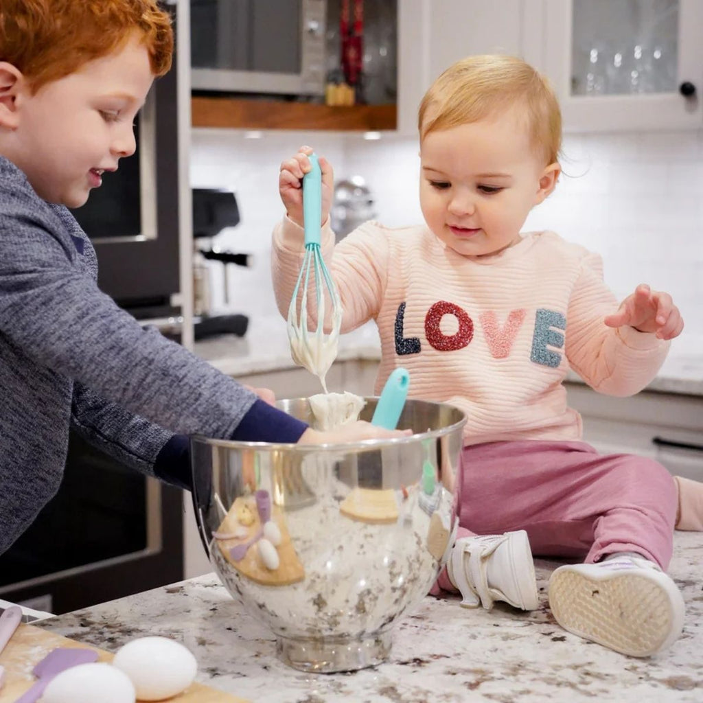 Two children in a kitchen, one with red hair and the other with blonde hair, engaging in cooking activities.