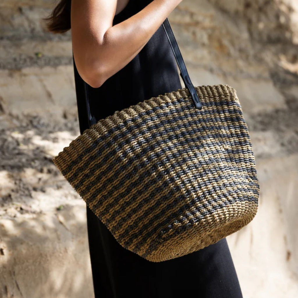Person holding a woven handbag against a stone wall background