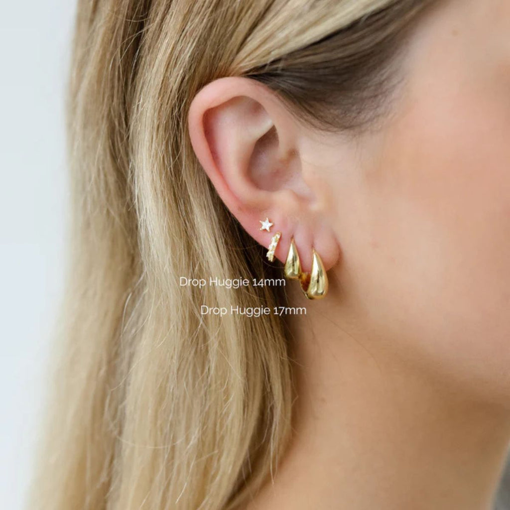 Close-up of an ear wearing gold earrings with text indicating earring sizes.