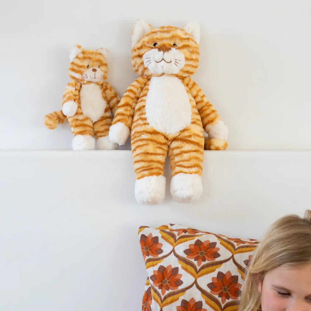 Two plush cat toys on a white surface with a child partially visible at the bottom right corner.