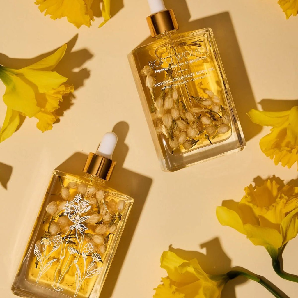 Two glass bottles with gold caps and floral designs on a beige background with yellow flowers.