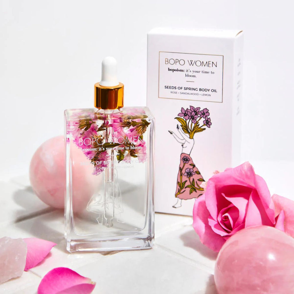 Bopo Women body oil bottle with packaging and pink roses on a white background