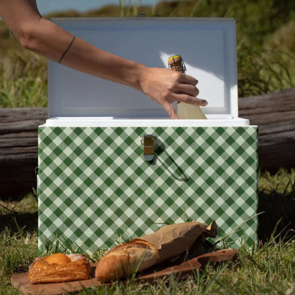Green and white checkered cooler with a hand reaching in to open it, surrounded by grass and a wooden log.