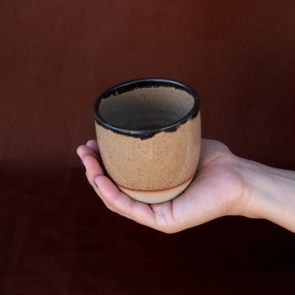 Hand holding a ceramic cup with a brown background