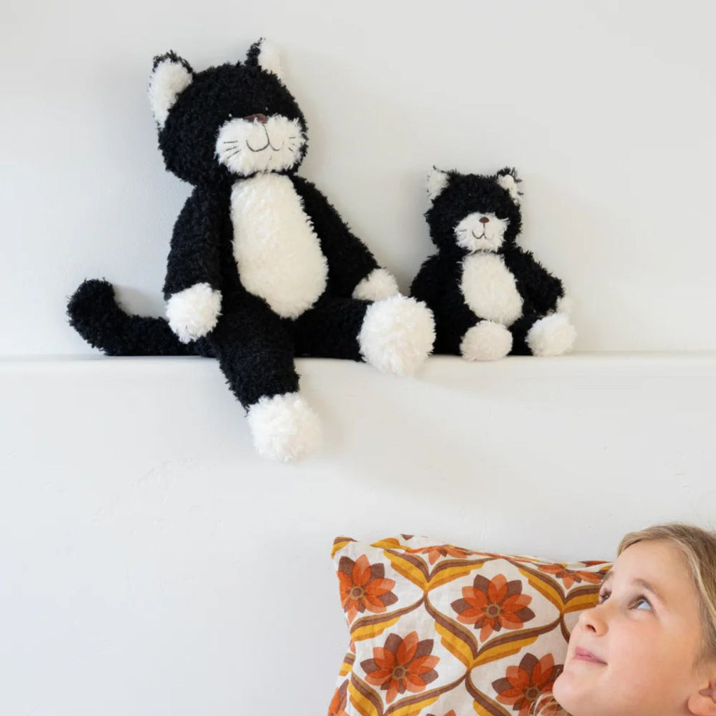 Two black and white cat-shaped plush toys on a white surface with a child looking at them.