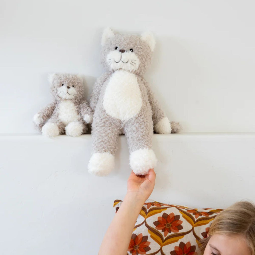 Two plush toys resembling cats on a white surface with a child's hand reaching out.