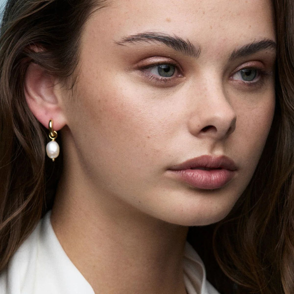 Close-up of a woman wearing pearl earrings with a neutral background