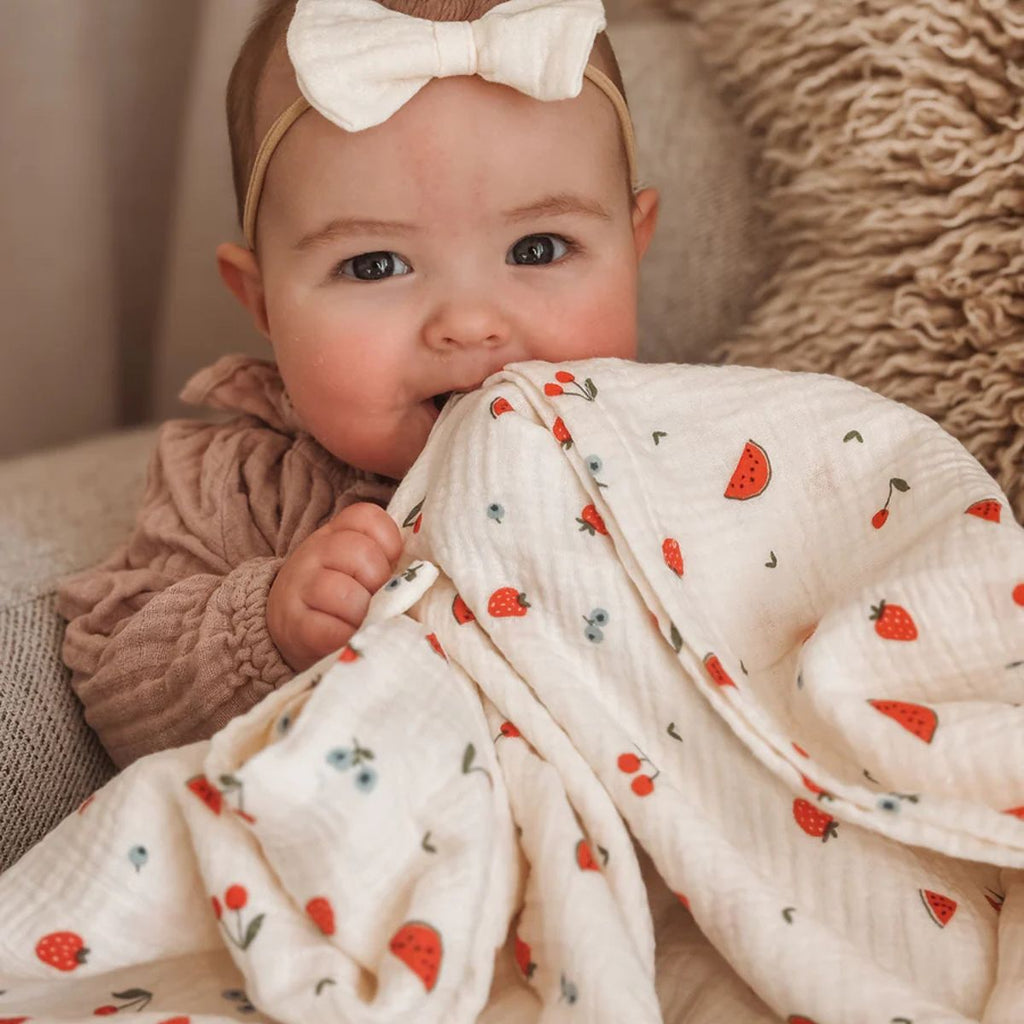 Baby wrapped in a blanket with strawberry pattern, wearing a white bow headband.