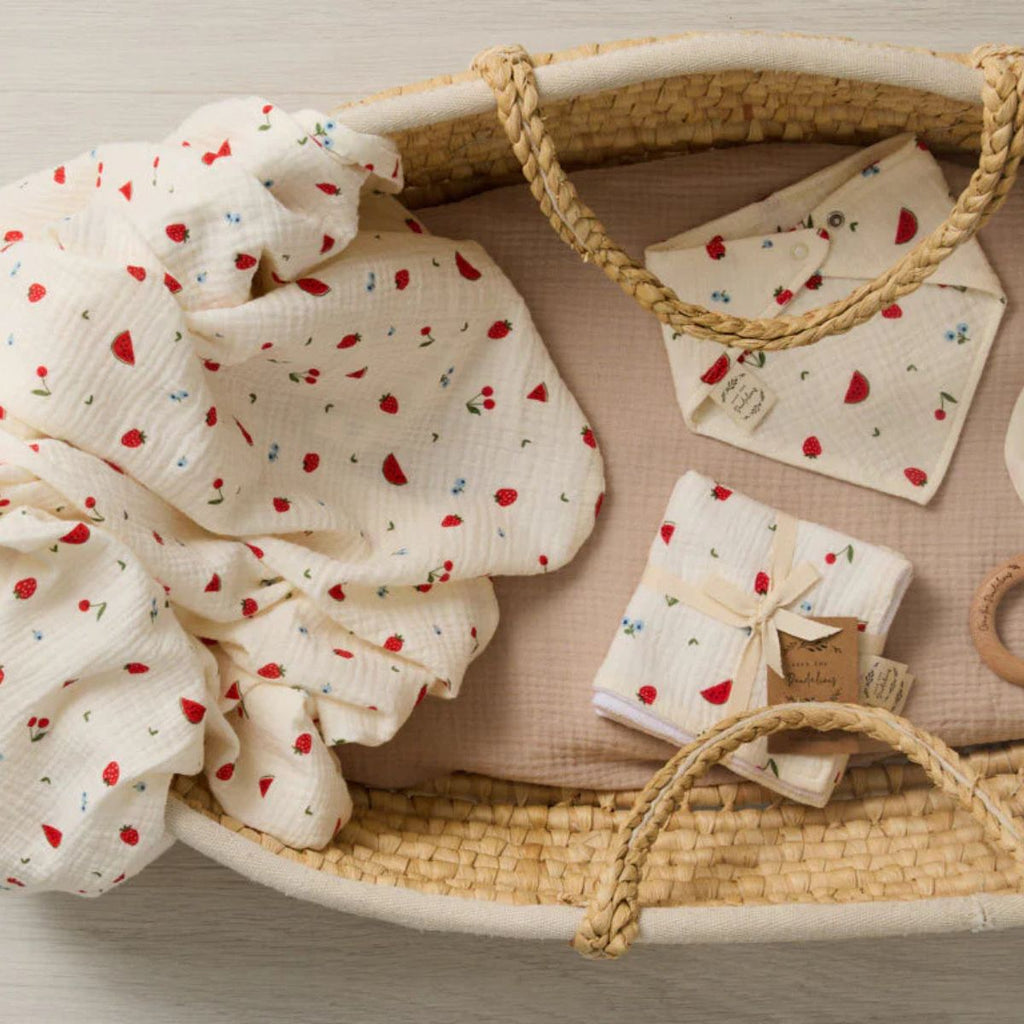 Baby swaddle and items in a woven basket with a neutral background