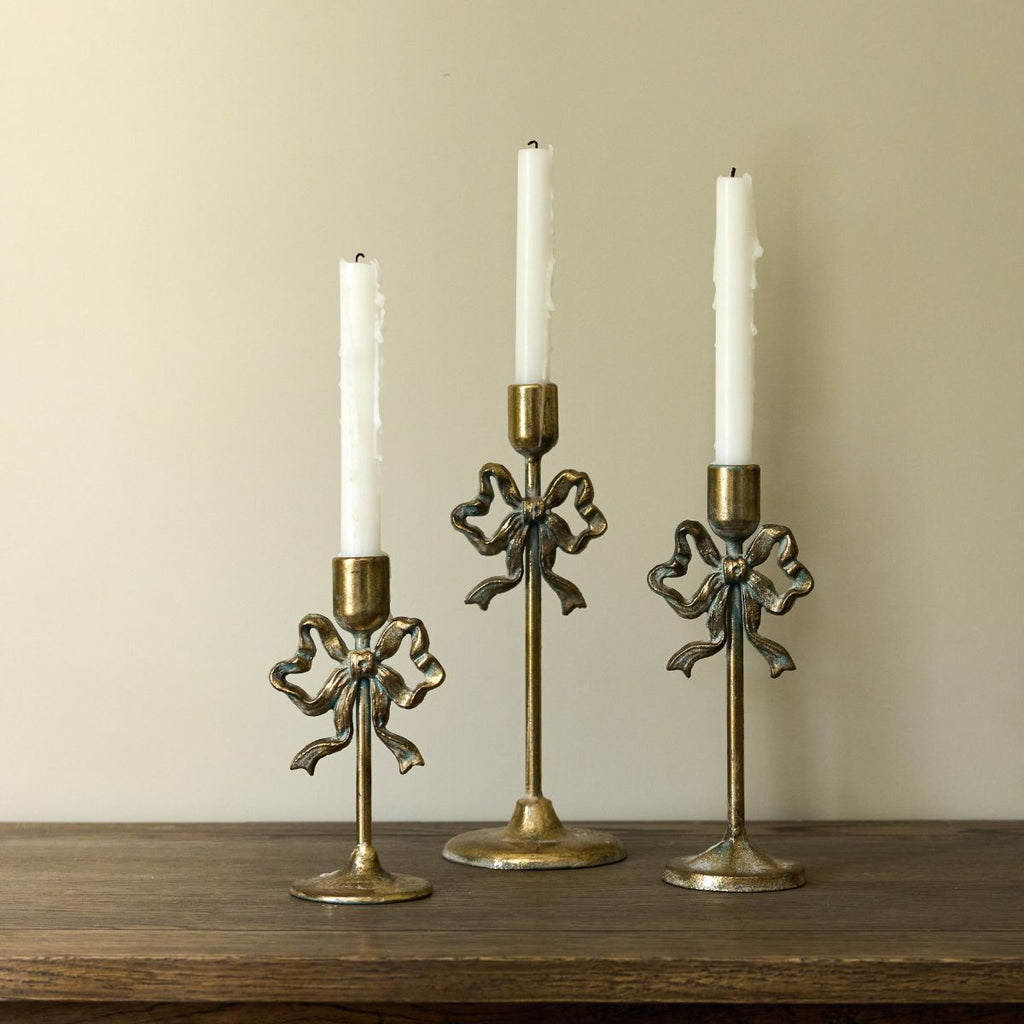 Three decorative candle holders with candles on a wooden surface against a beige wall.