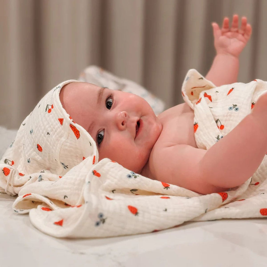 Baby wrapped in a white hooded towel with red and black patterns, lying on a bed.