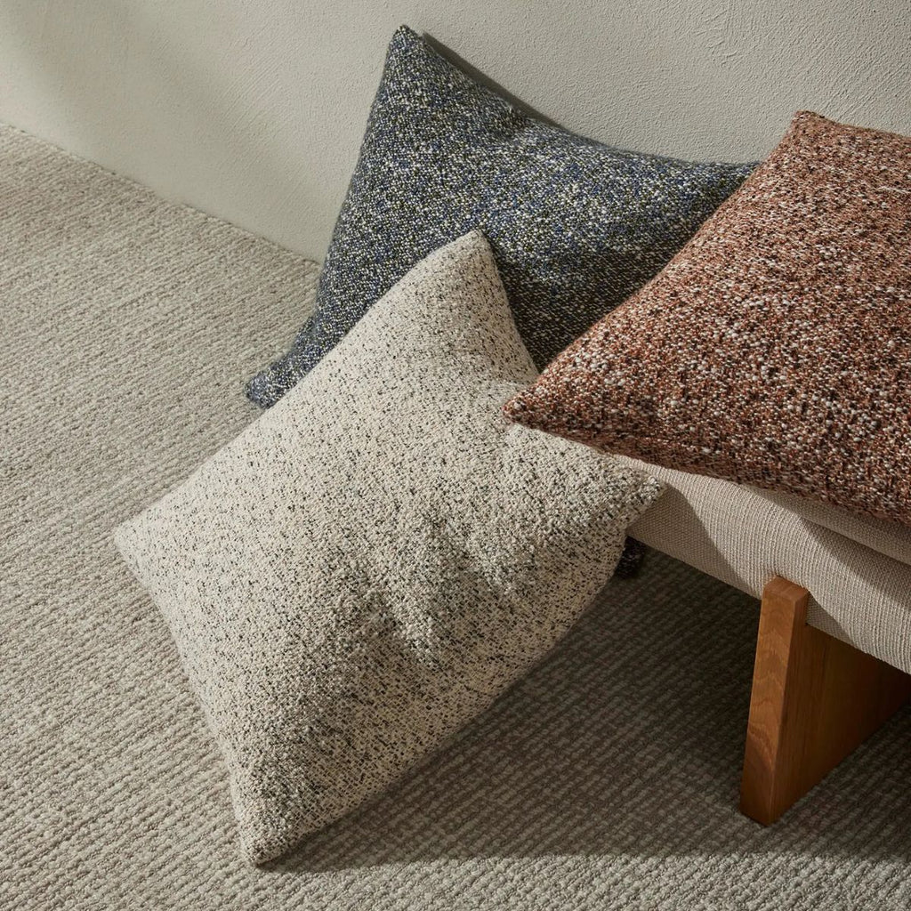 Three textured pillows in gray, brown, and beige on a sofa.