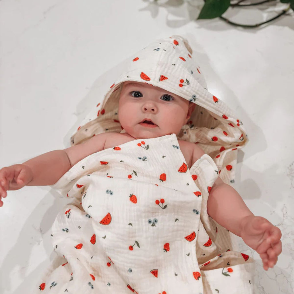 Baby wrapped in a hooded towel with red patterns, wearing a matching headband on a white background.