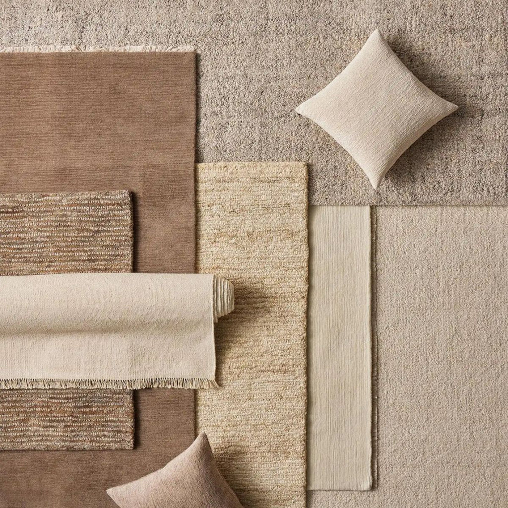 Collection of beige and brown textured rugs and cushions on a neutral background