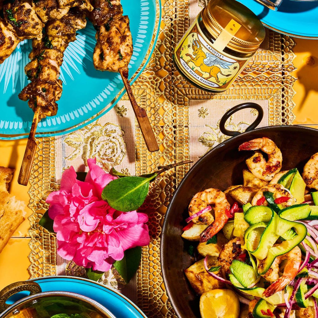 Diverse food items including skewers, a bowl of salad, and a jar of honey on a decorative tablecloth.