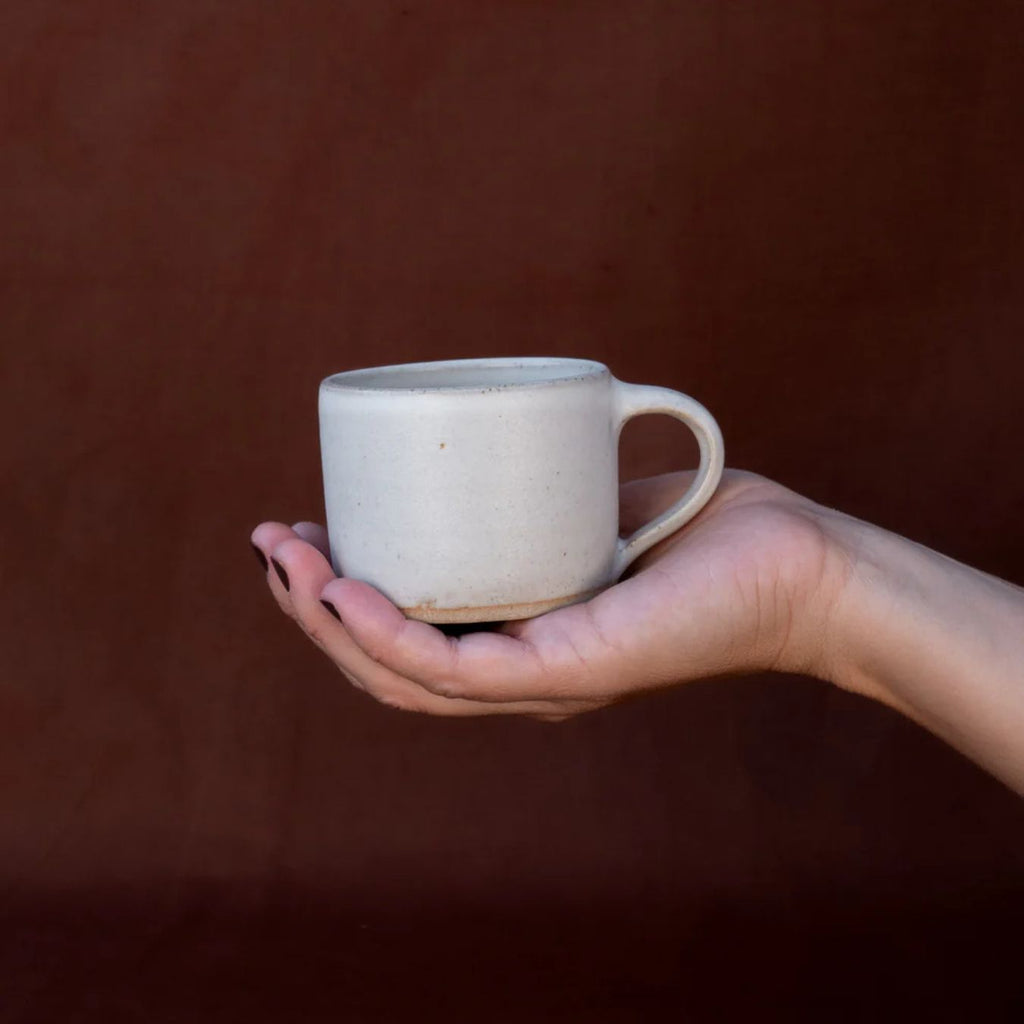 Hand holding a ceramic mug against a brown background