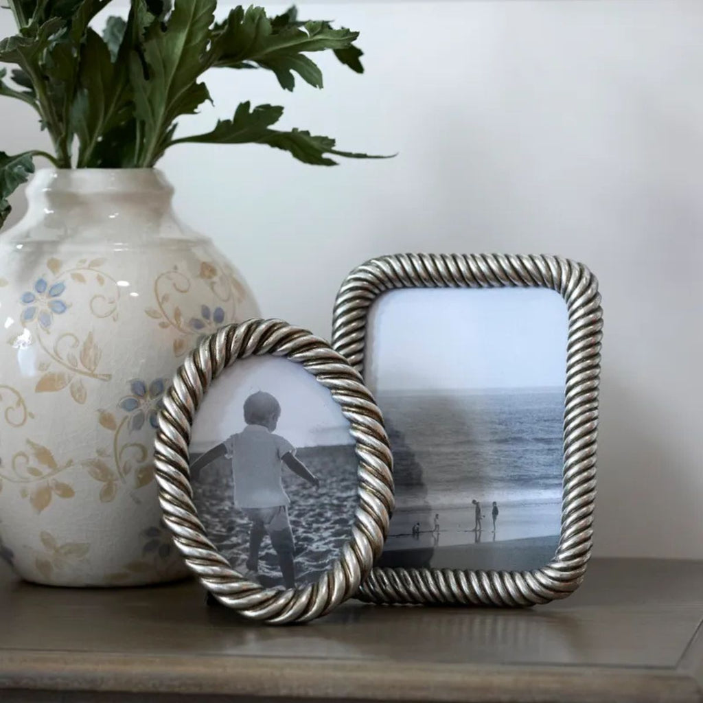 Two decorative photo frames with a vase and plant on a surface.