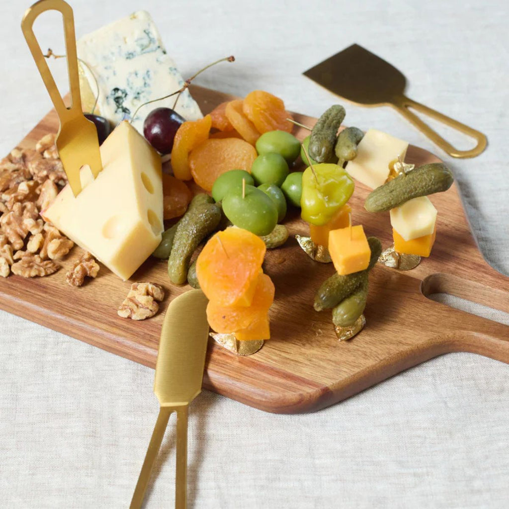 Wooden cutting board with assorted cheeses, dried fruits, and nuts on a white background