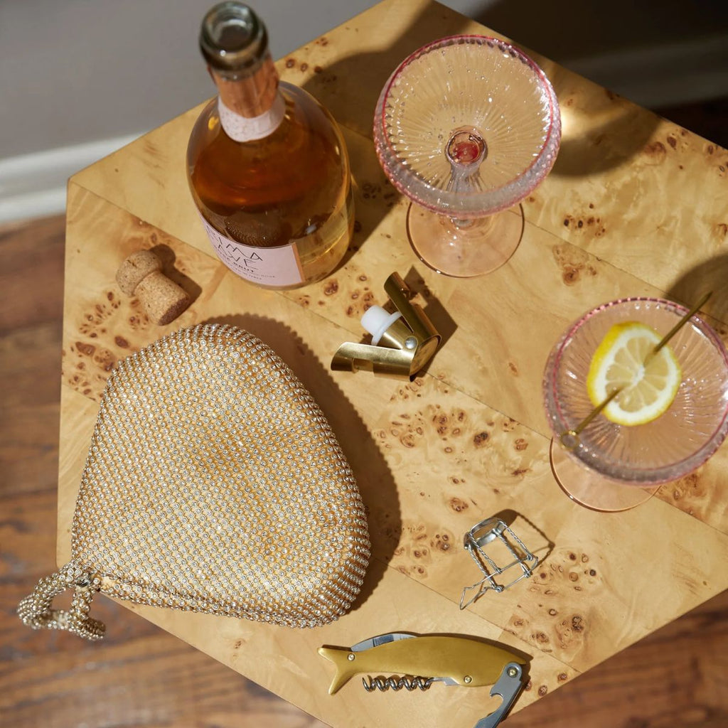 Gold mesh handbag, bottle, and glasses on a wooden surface