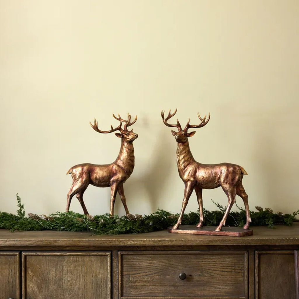 Two bronze deer statues on a wooden surface with a beige wall background