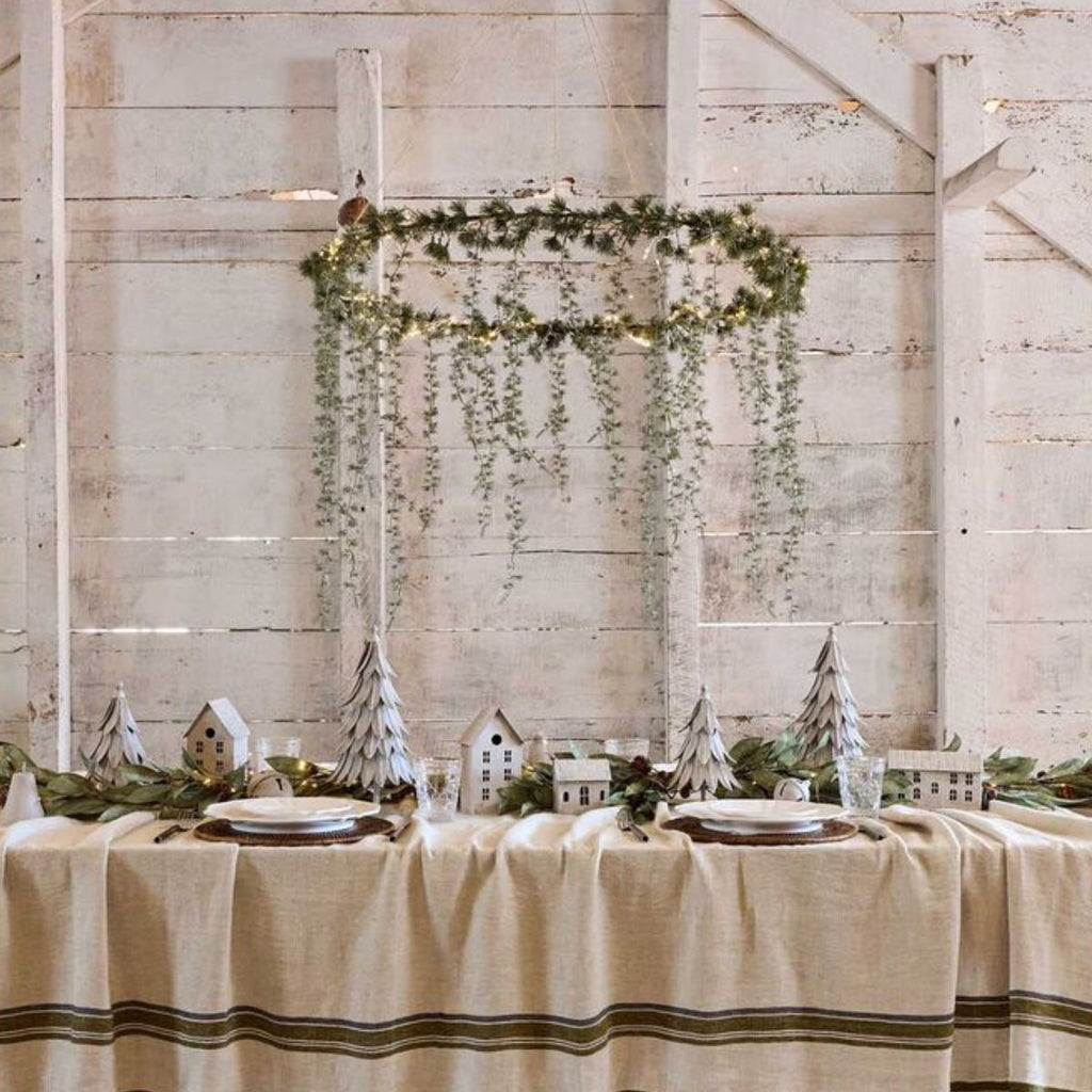 Table setting with Christmas decorations against a wooden wall with greenery and lights.