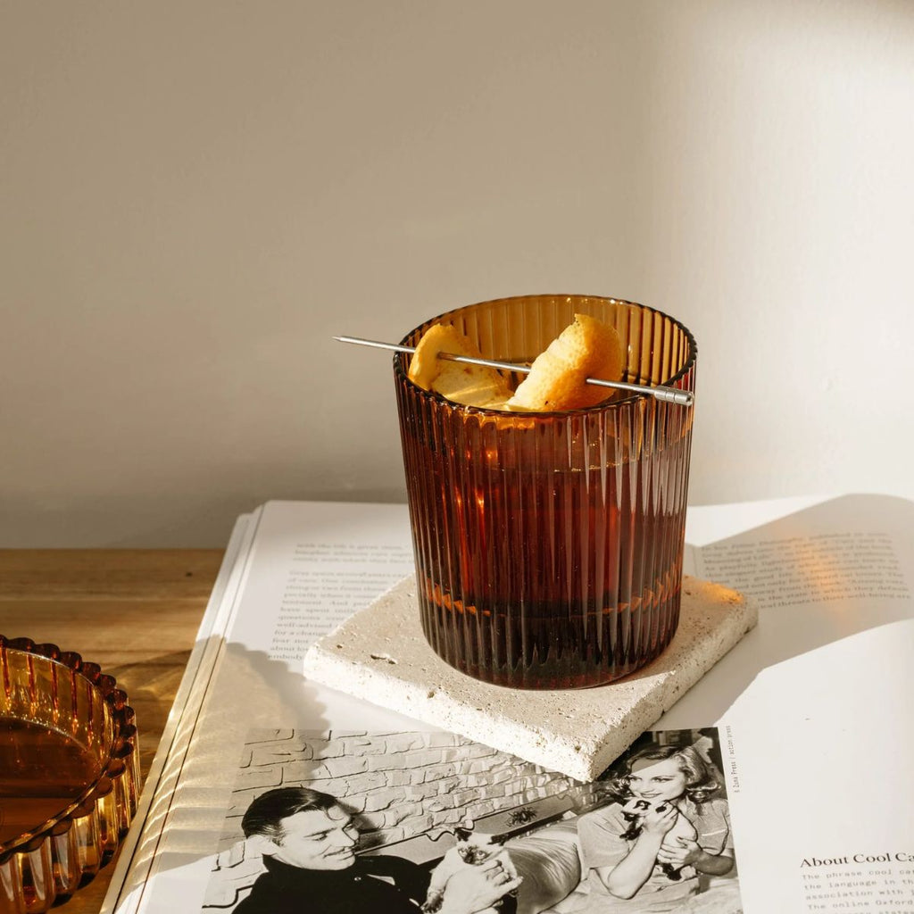 Brown cocktail in a textured glass with a skewer on top, placed on an open book.
