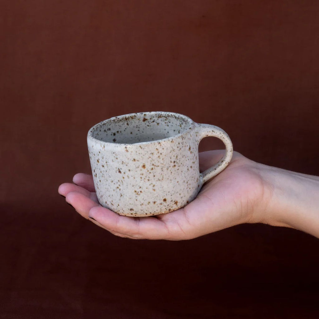 Hand holding a speckled ceramic mug against a brown background