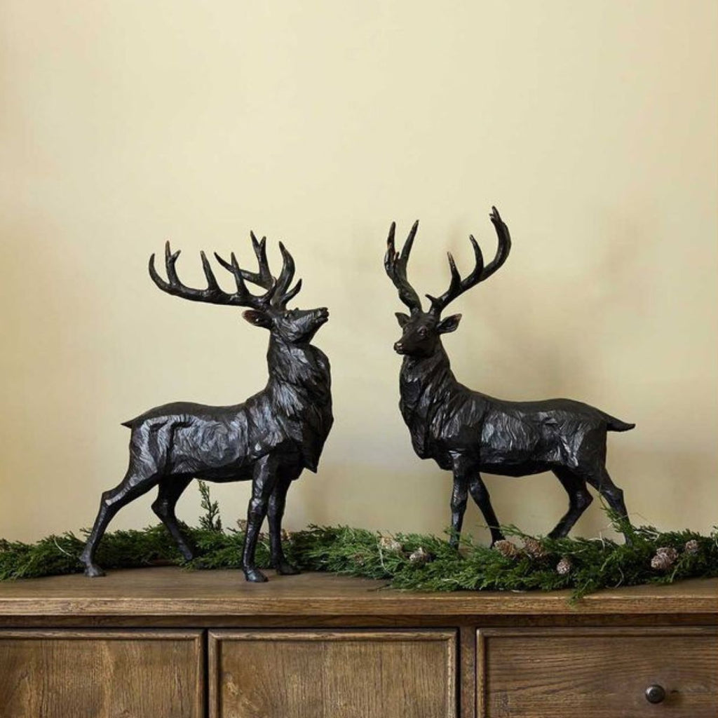 Two black deer statues on a wooden surface with a beige wall background