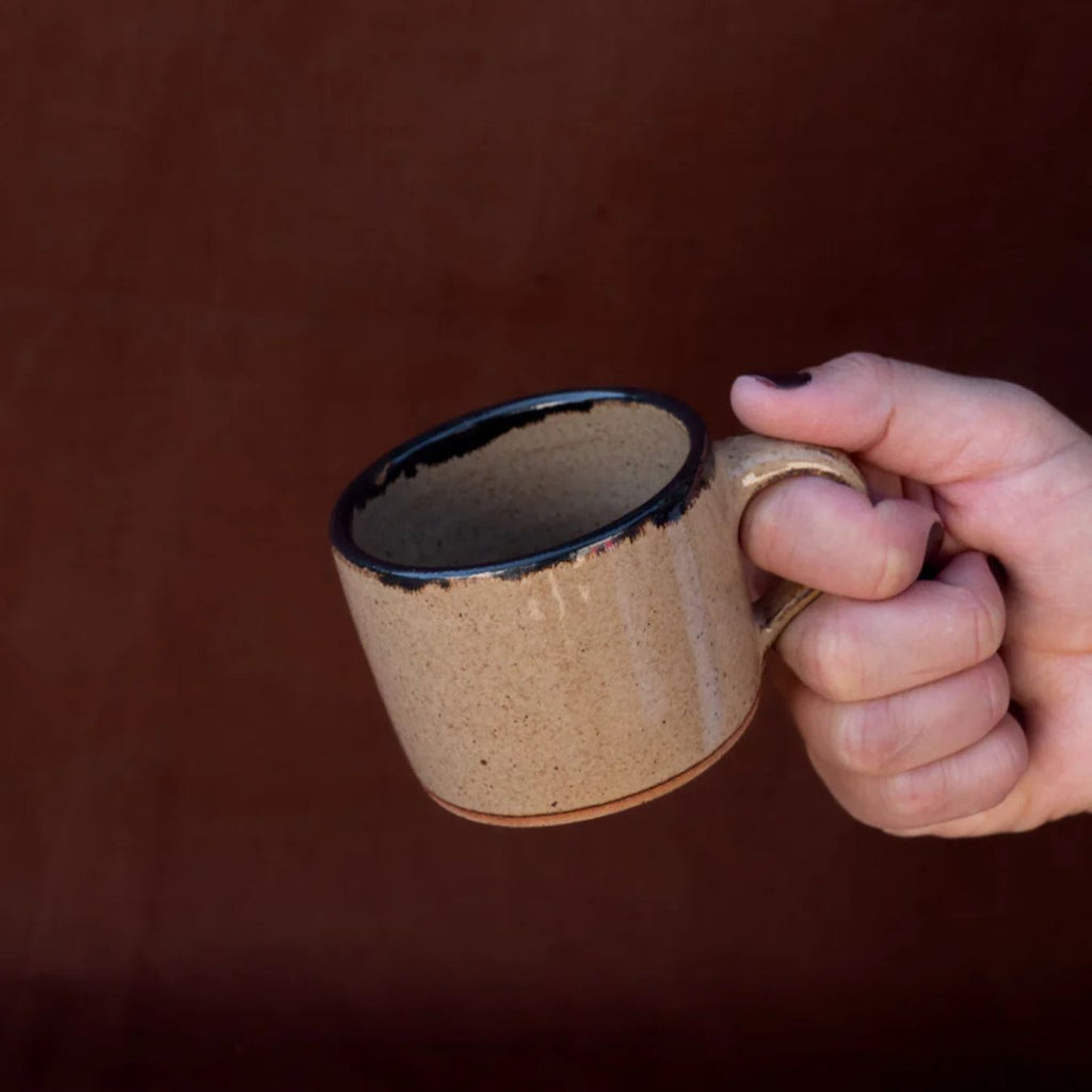 Hand holding a brown ceramic mug against a dark background