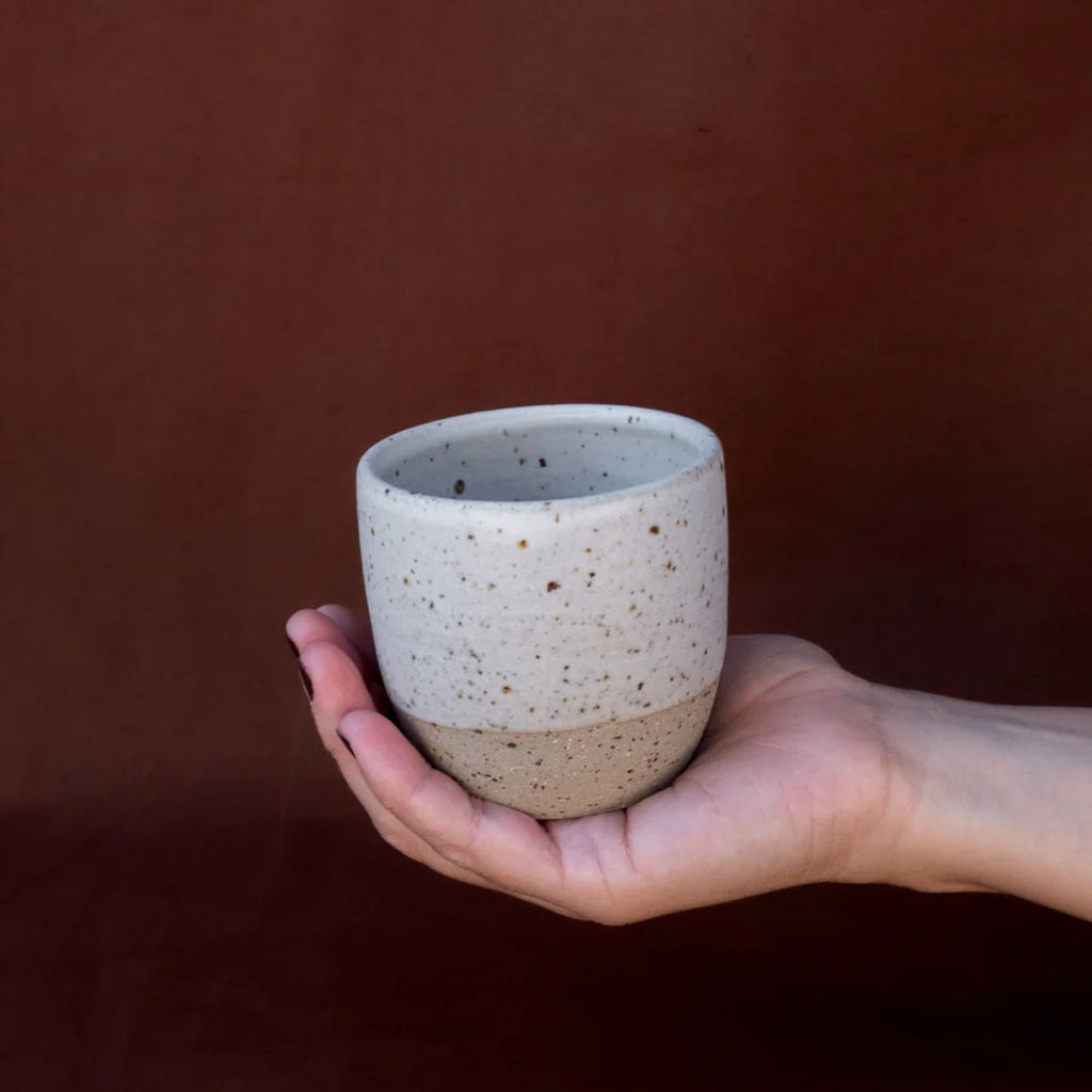 Hand holding a speckled ceramic cup against a brown background