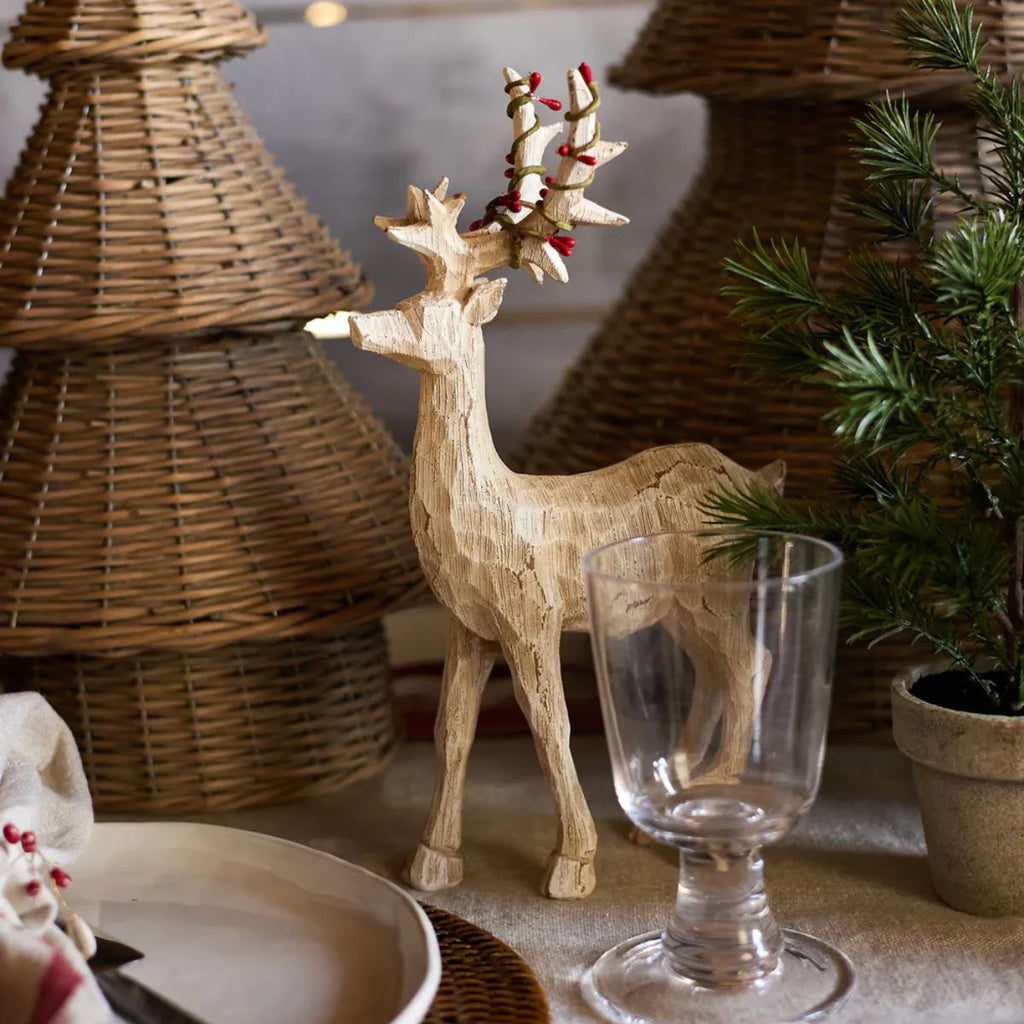 Wooden reindeer decoration with a glass on a table with wicker baskets and plants.