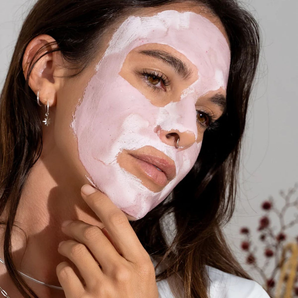 Woman applying a pink facial mask with a neutral background