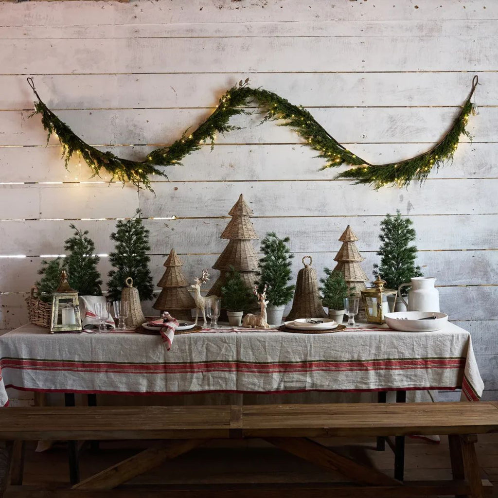 Decorated table with Christmas trees and lanterns against a wooden wall with a garland.
