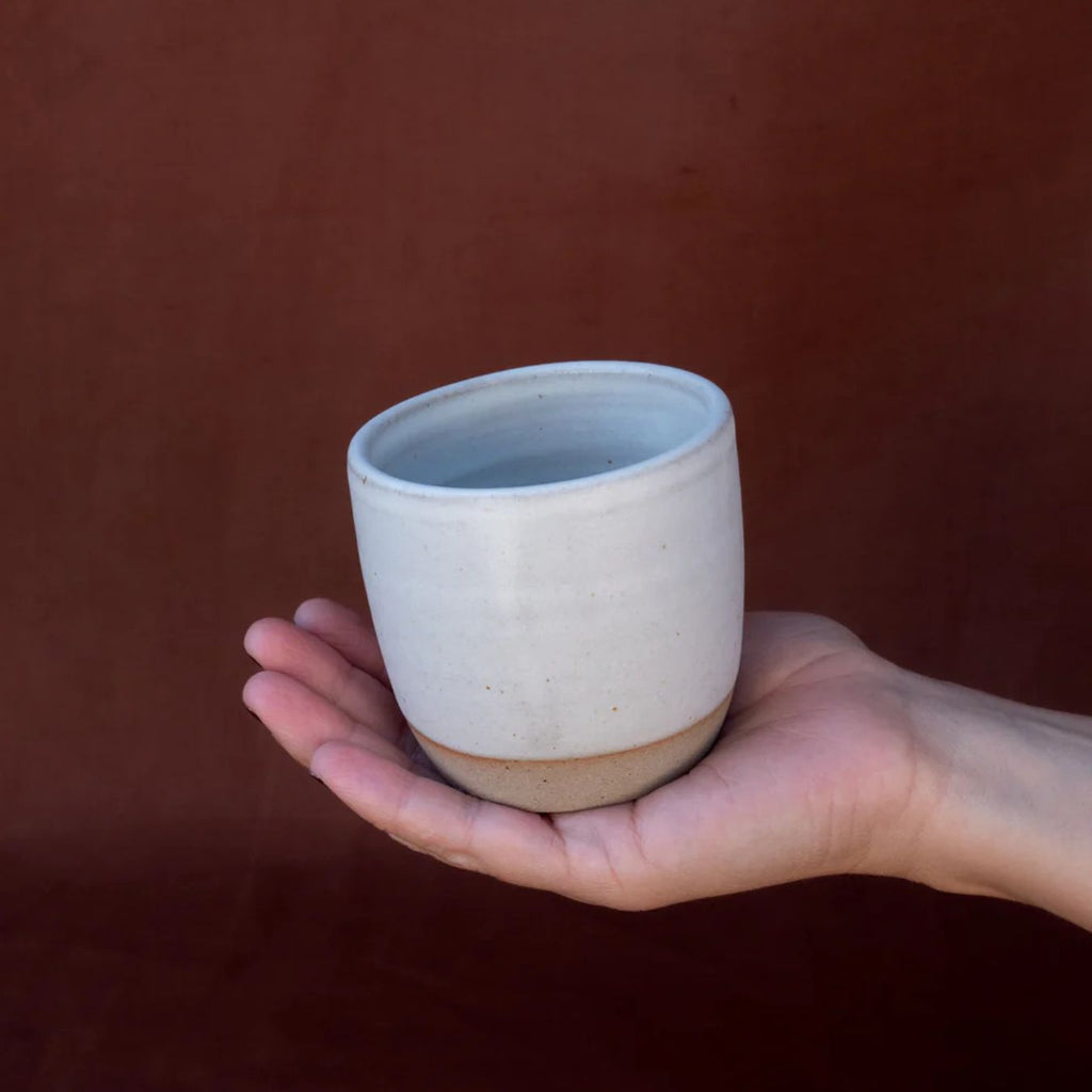 Hand holding a ceramic cup against a brown background
