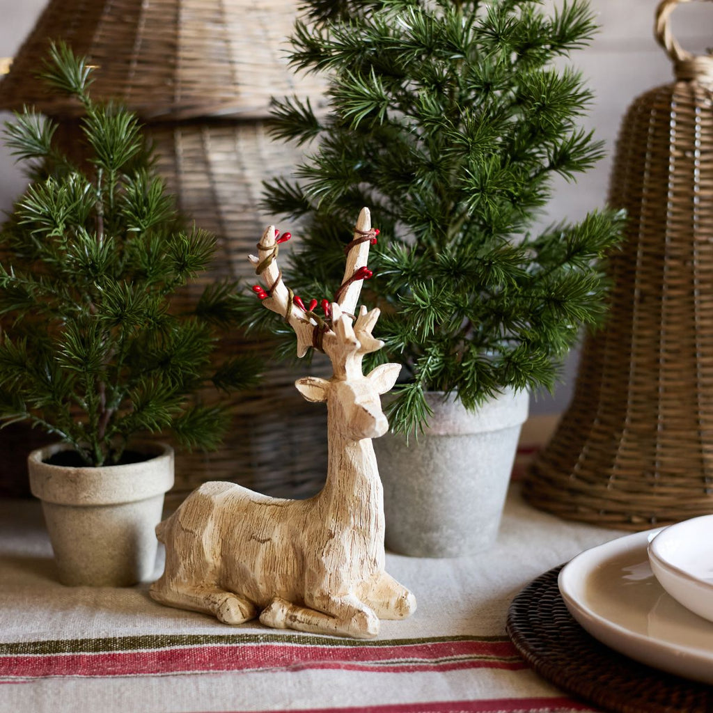 Decorative wooden deer figurine with red berries on a table with plants and wicker baskets.