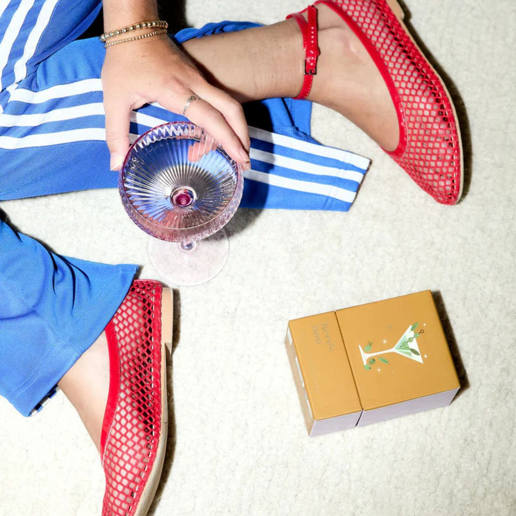 Person wearing red shoes with blue shorts, holding a glass with a straw, and a small box on a light surface.