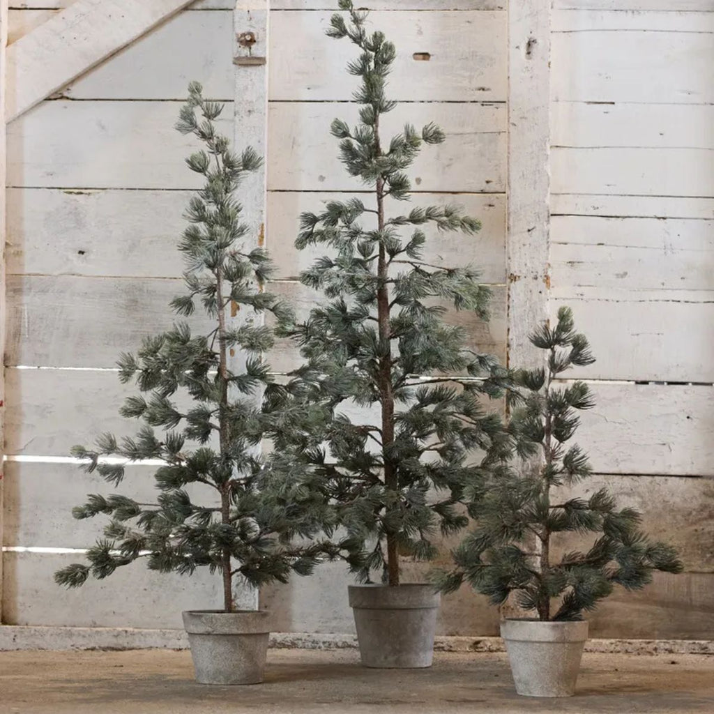Three potted artificial trees against a wooden wall.