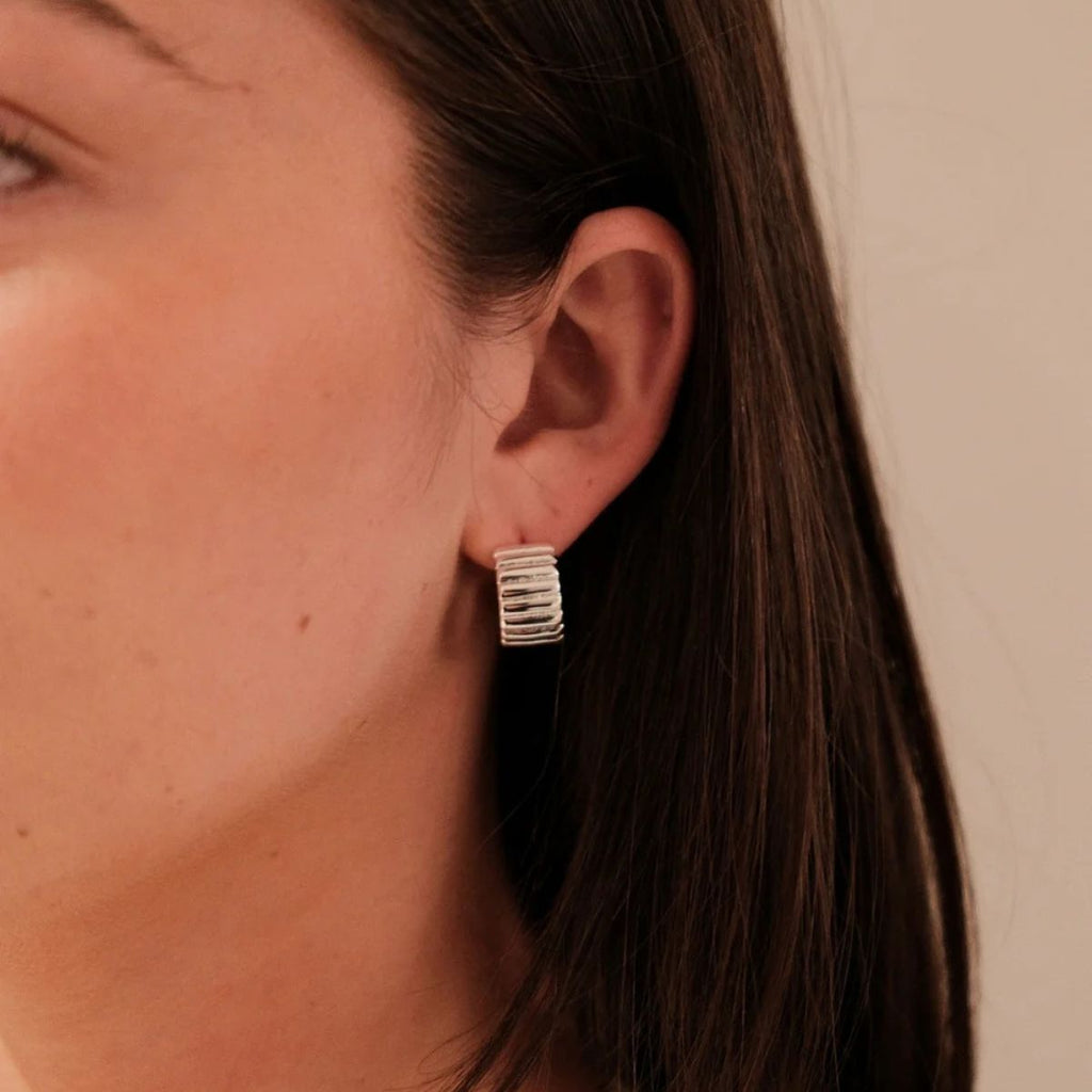 Close-up of an ear wearing a silver hoop earring with a neutral background