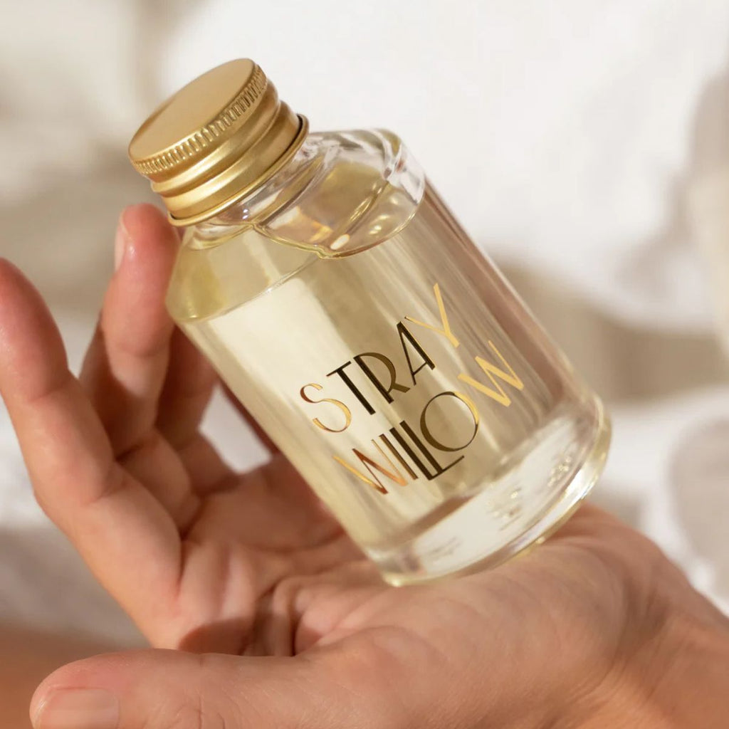 Hand holding a small bottle with a gold cap labeled 'Strawflower' against a blurred background.