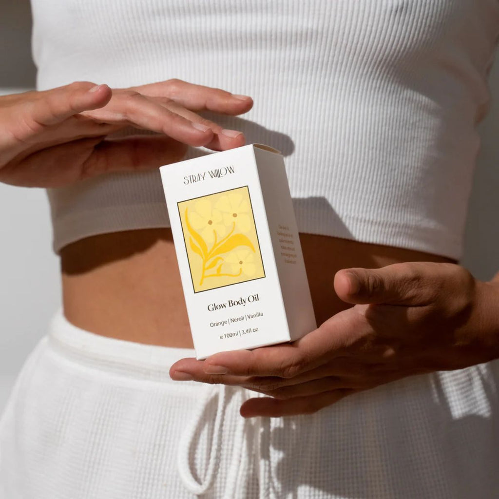 Person holding a box of Glow Body Oil by Stray Willow against a neutral background