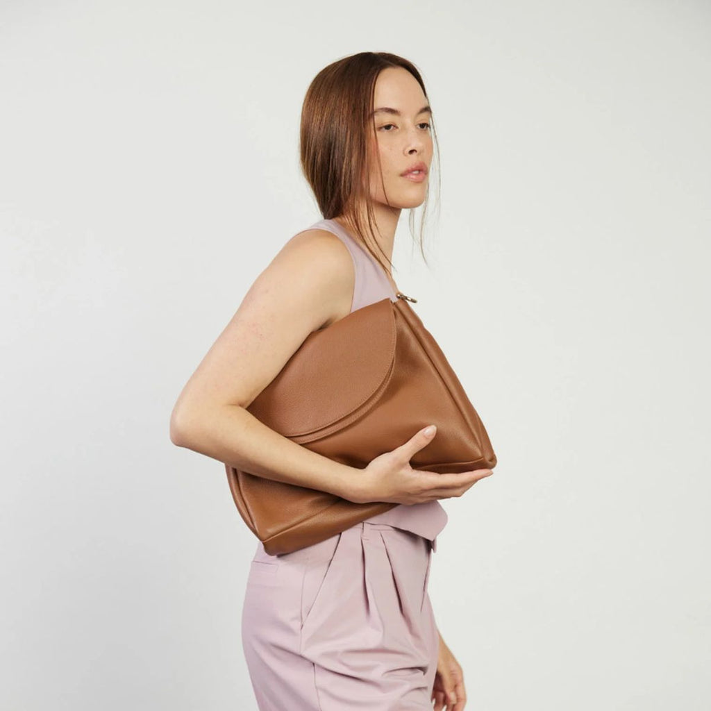 Woman holding a brown leather bag against a plain background